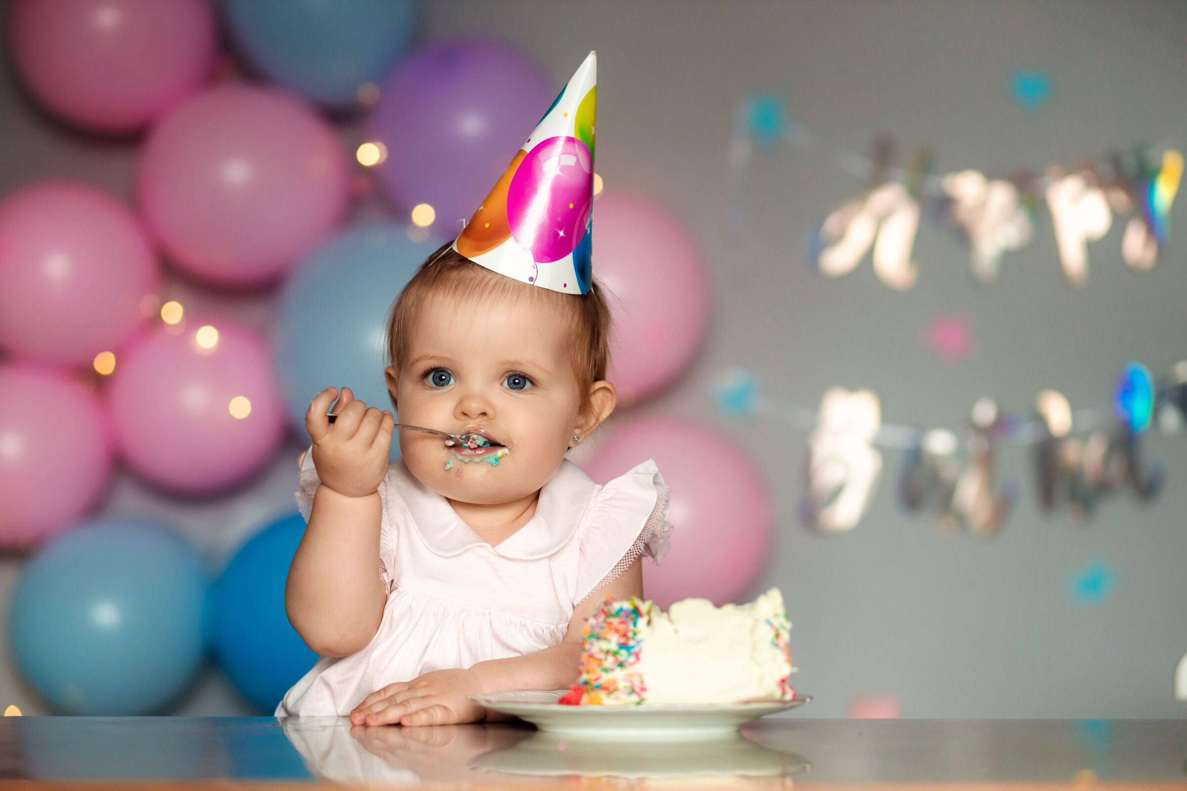 Toddler in a party hat enjoys a slice of cake under a Happy&nbsp;Birthday banner at a Chuck&nbsp;E.&nbsp;Cheese party room.