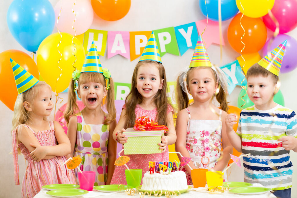 Kids ages 5–8 celebrate in Chuck&nbsp;E.&nbsp;Cheese party room with birthday cake, decorations, and arcade games in background.