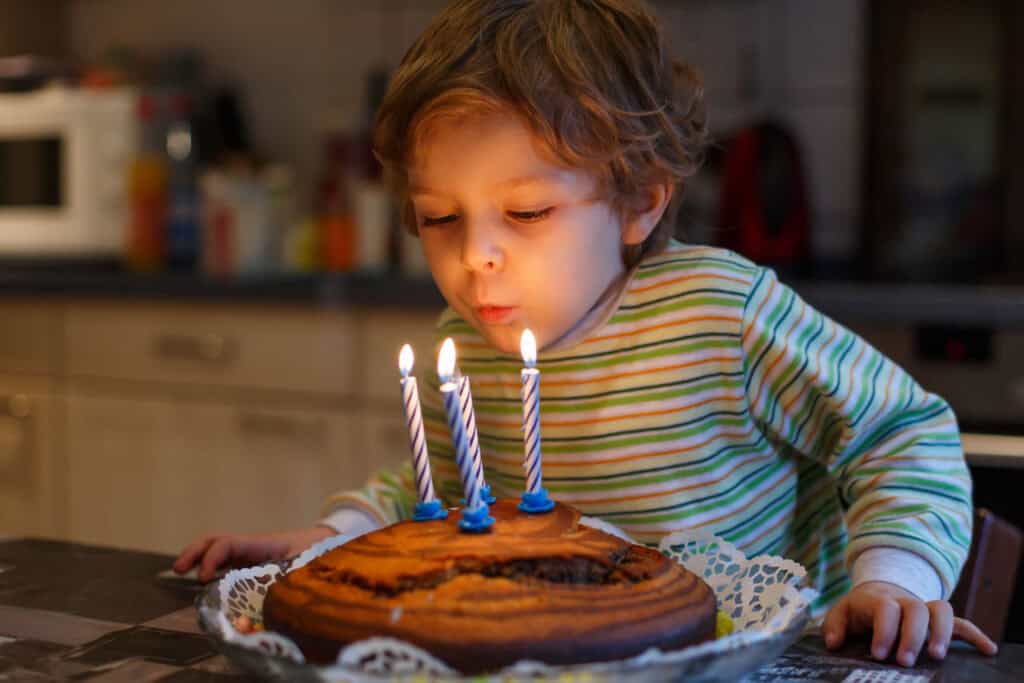 Birthday party in the party room: child (age 4–6) blows out candles on cake, family watching.