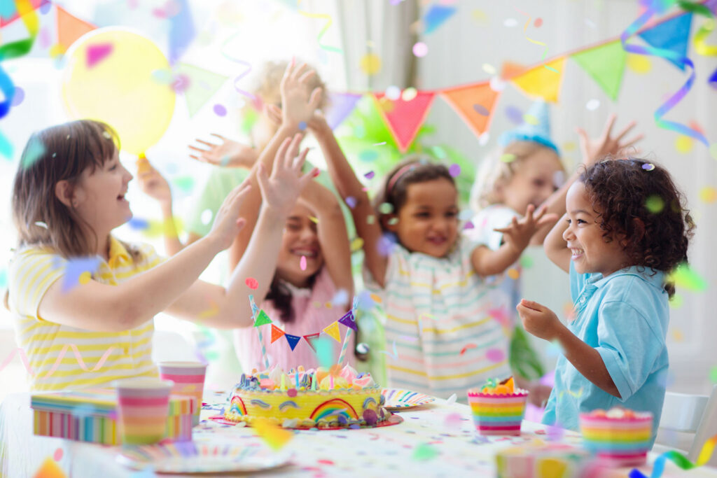 Birthday party in Chuck&nbsp;E.&nbsp;Cheese party room with smiling kids (ages 5–8), balloons, pizza, decorated cake, and arcade games.