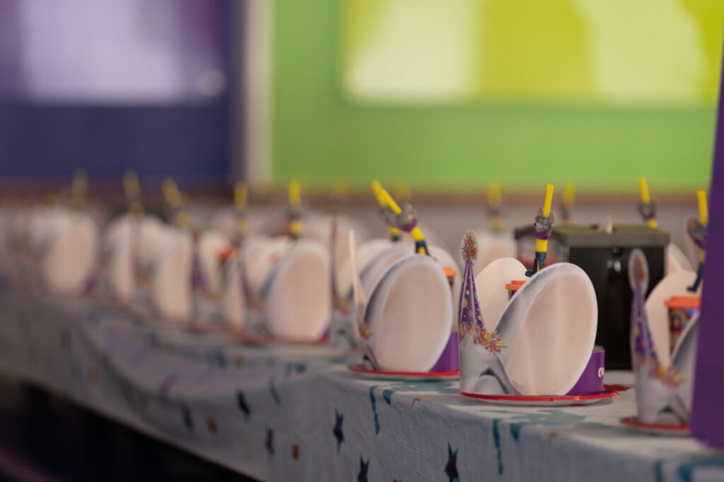 Birthday party table set with Chuck E. Cheese themed plates, cups, and party hats.