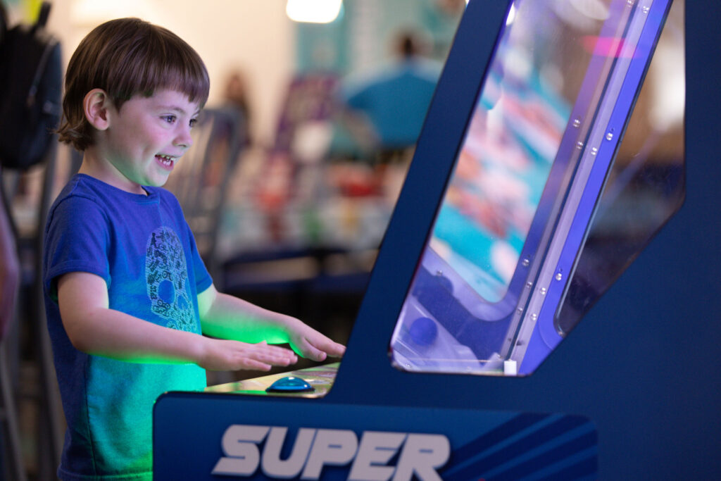Boy smiling playing an arcade game at Chuck E. Cheese.