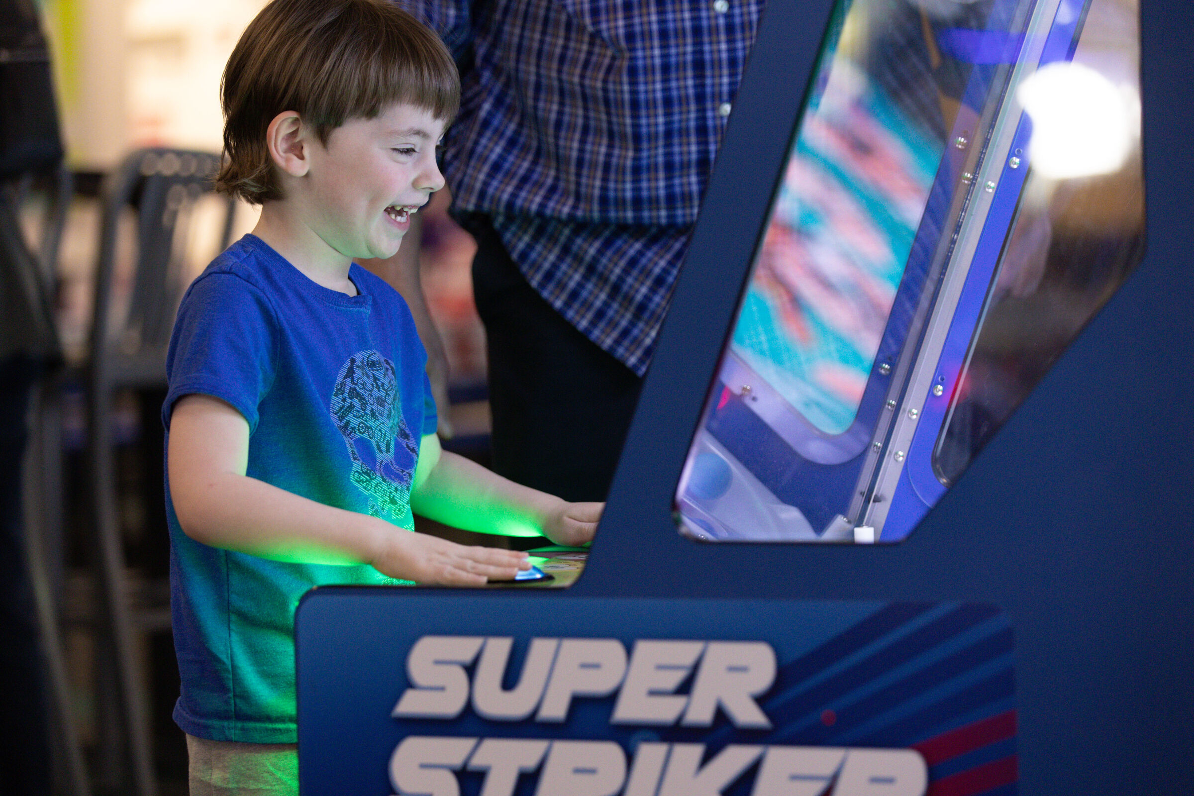 Joyful boy playing an arcade game at Chuck E. Cheese with hands on illuminated controls