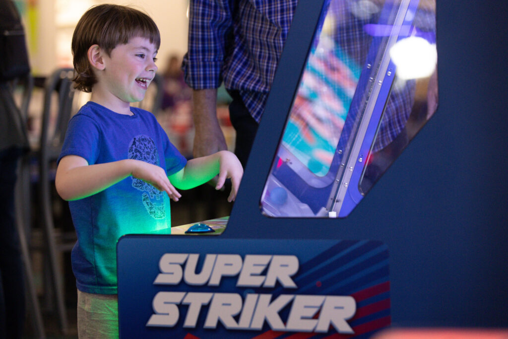 Joyful boy playing the Super Striker arcade game at Chuck E. Cheese at a Sensory Sensitive Sunday event.