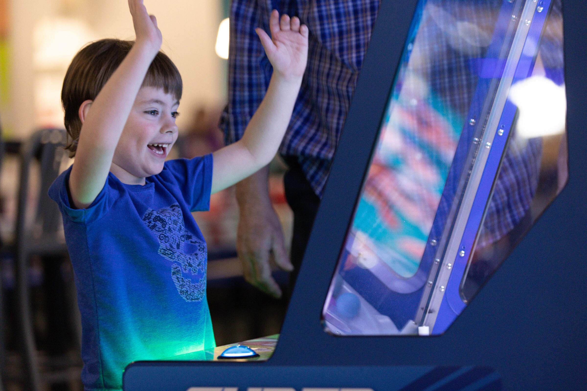 Joyful child with arms raised in triumph playing an arcade game at Chuck E. Cheese