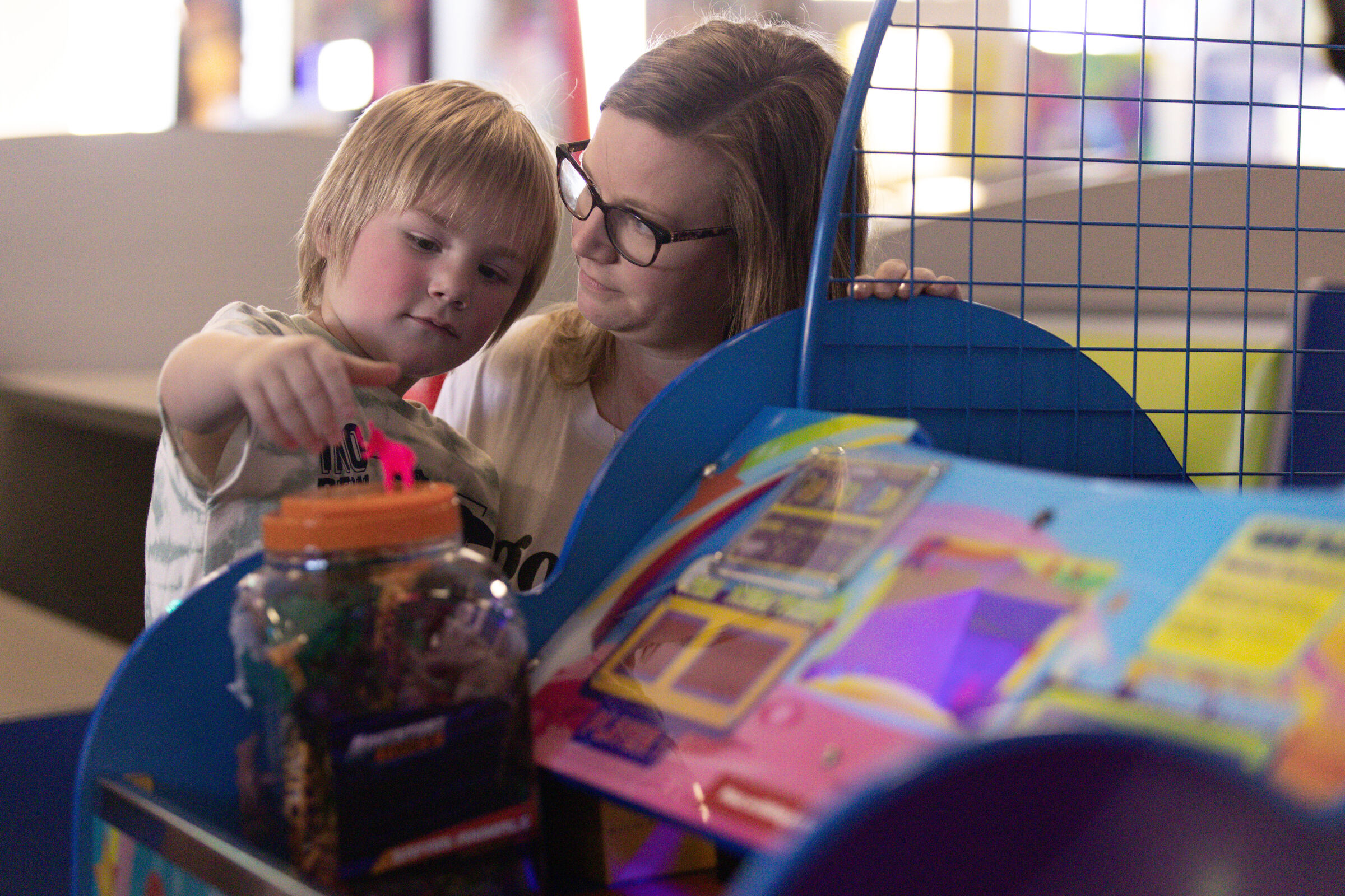 Child and adult playing an arcade game together at Chuck E. Cheese, reaching together for the prize slot.