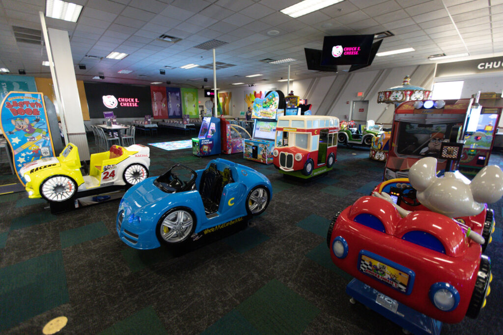 Arcade floor at Chuck E. Cheese with car-themed kiddie rides and games at a Sensory Sensitive Sunday event.