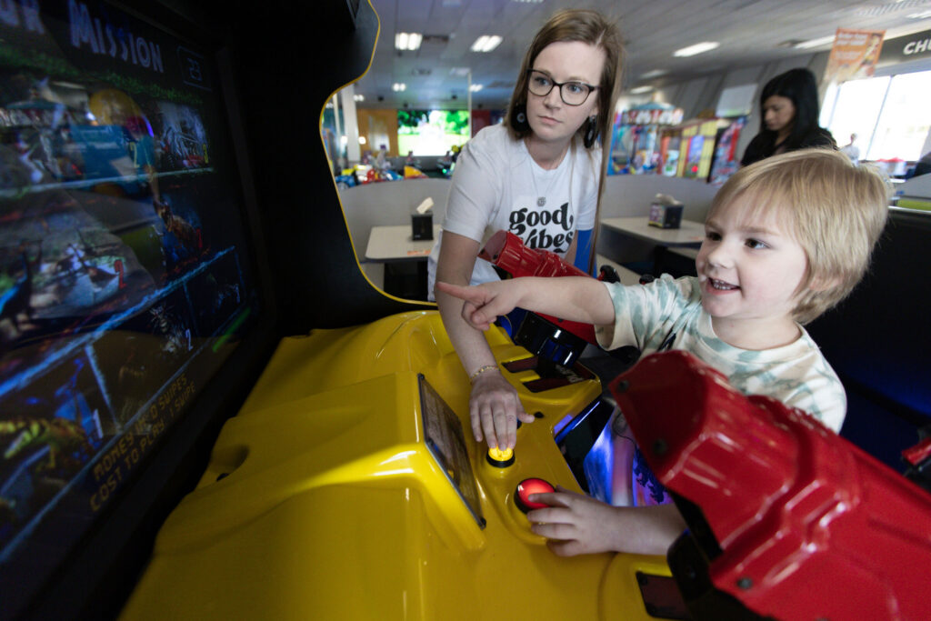 Mom and young child playing an arcade racing game together at Chuck E. Cheese at a Sensory Sensitive Sunday event.