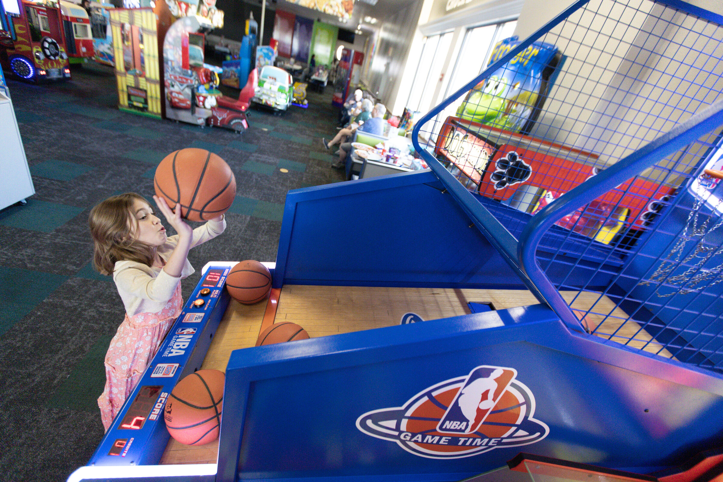 Girl playing an NBA basketball arcade game at Chuck E. Cheese, aiming carefully