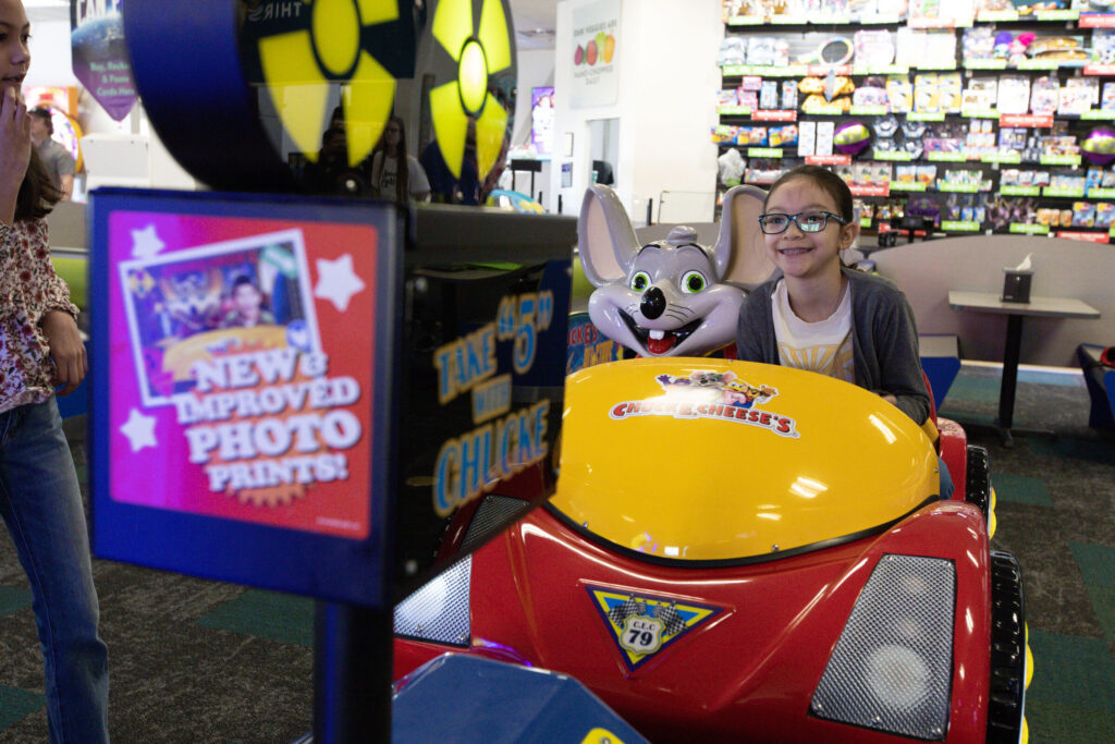 Girl smiling while sitting calmly in a Chuck E. Cheese ride-on car game at a Sensory Sensitive Sunday event.