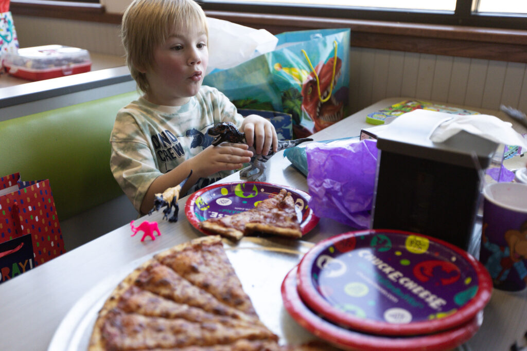 Young boy playing with dinosaur toys at a Chuck E. Cheese birthday party table.