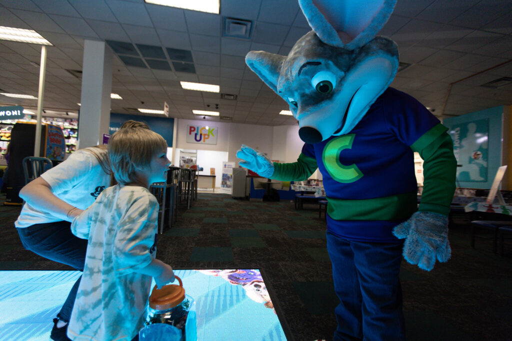 Chuck E. Cheese interacting with a child on an interactive floor game.