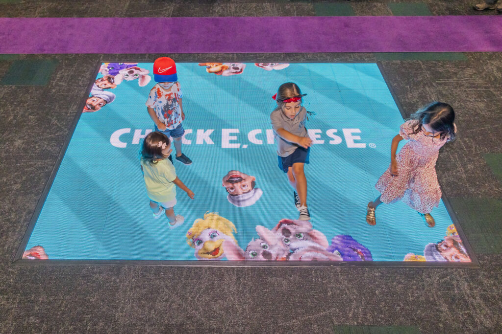 Kids playing on an interactive light-up dance floor at a Chuck E. Cheese location.
