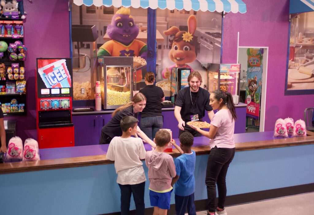 Chuck E. Cheese team members serving pizza and snacks to a group of excited kids.