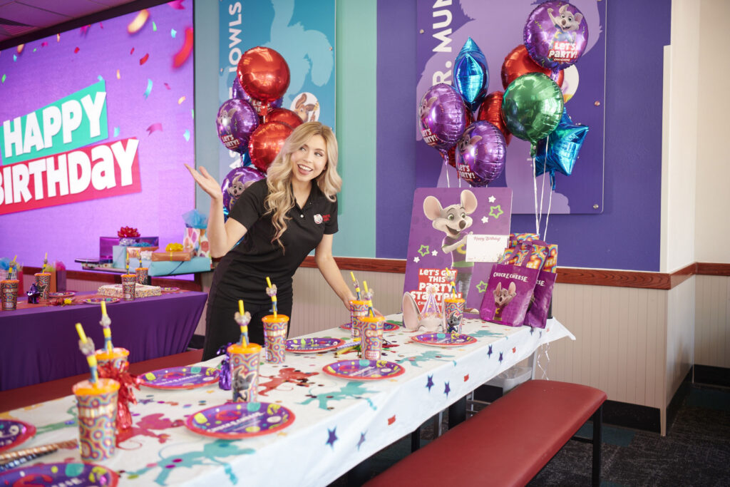 Chuck E. Cheese team member setting up a colorful birthday party table.