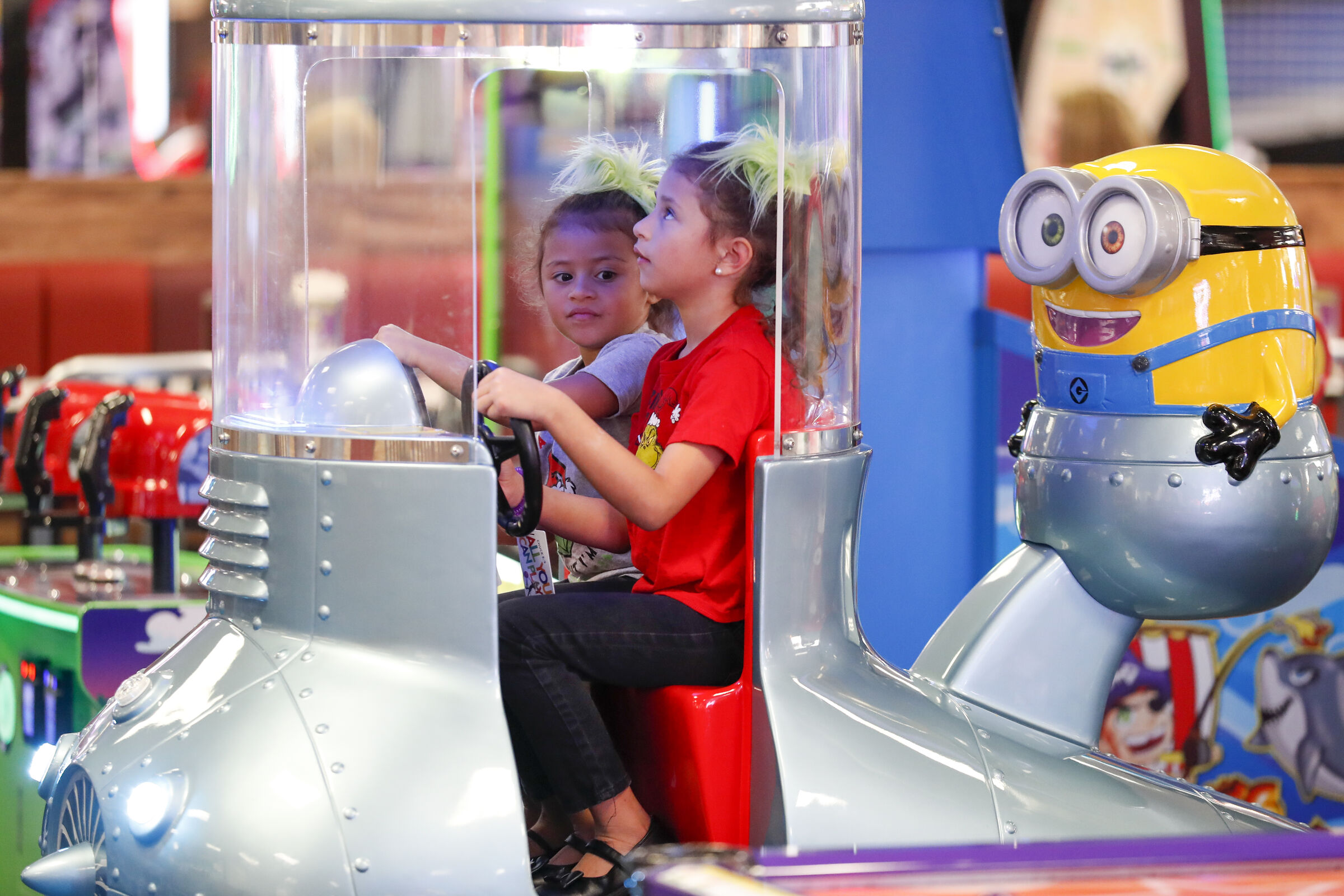 Two young girls playing together in a Minion-themed arcade game at Chuck E. Cheese.