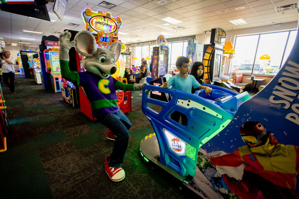 Kids ages 8-9 playing an arcade game at Chuck E. Cheese, competitive energy, neon glow