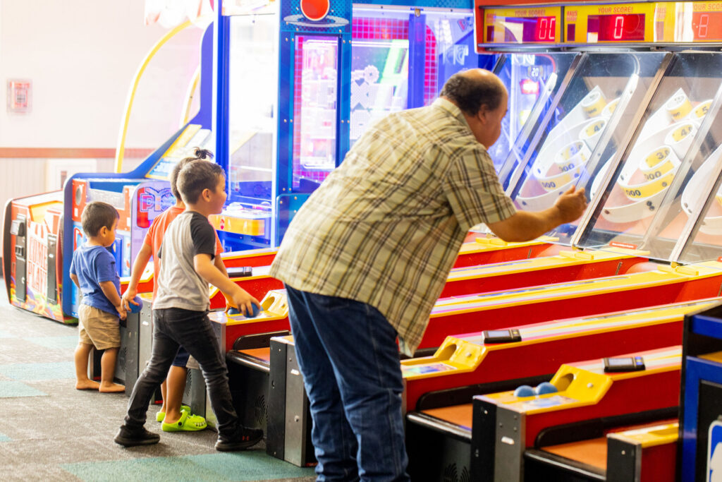 Grandfather and two young boys playing arcade games at Chuck E. Cheese.