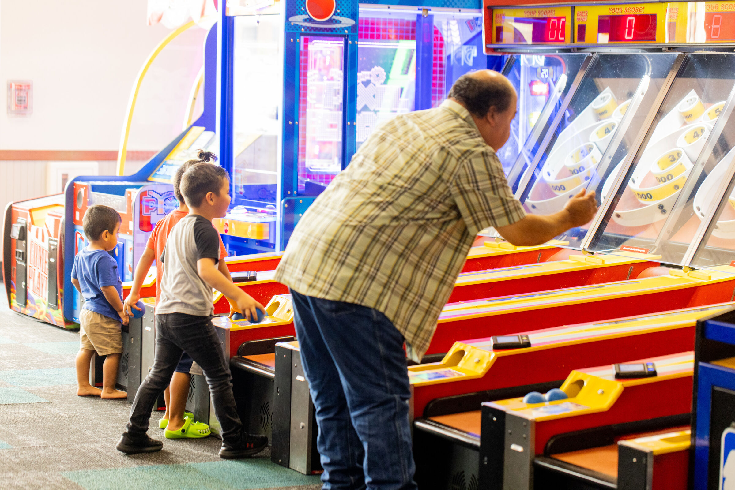 Grandfather and two young boys playing arcade games together at Chuck E. Cheese