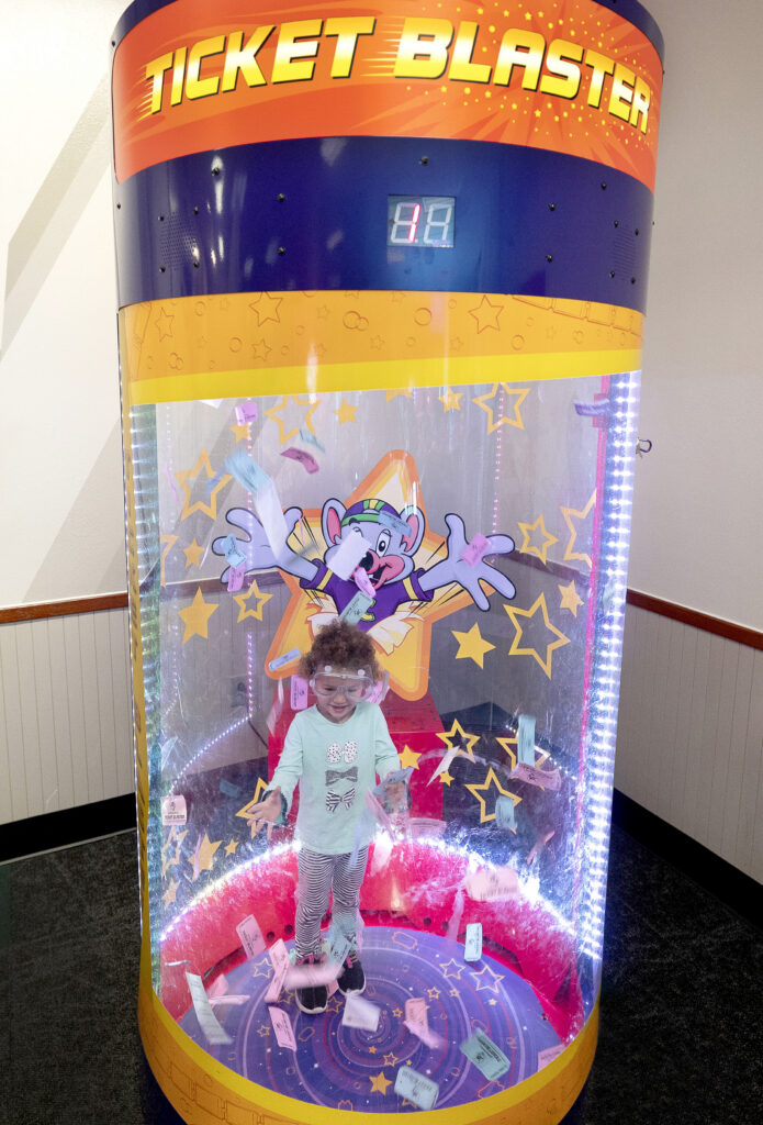 Young child in safety goggles catching tickets in the Ticket Blaster at Chuck E. Cheese.