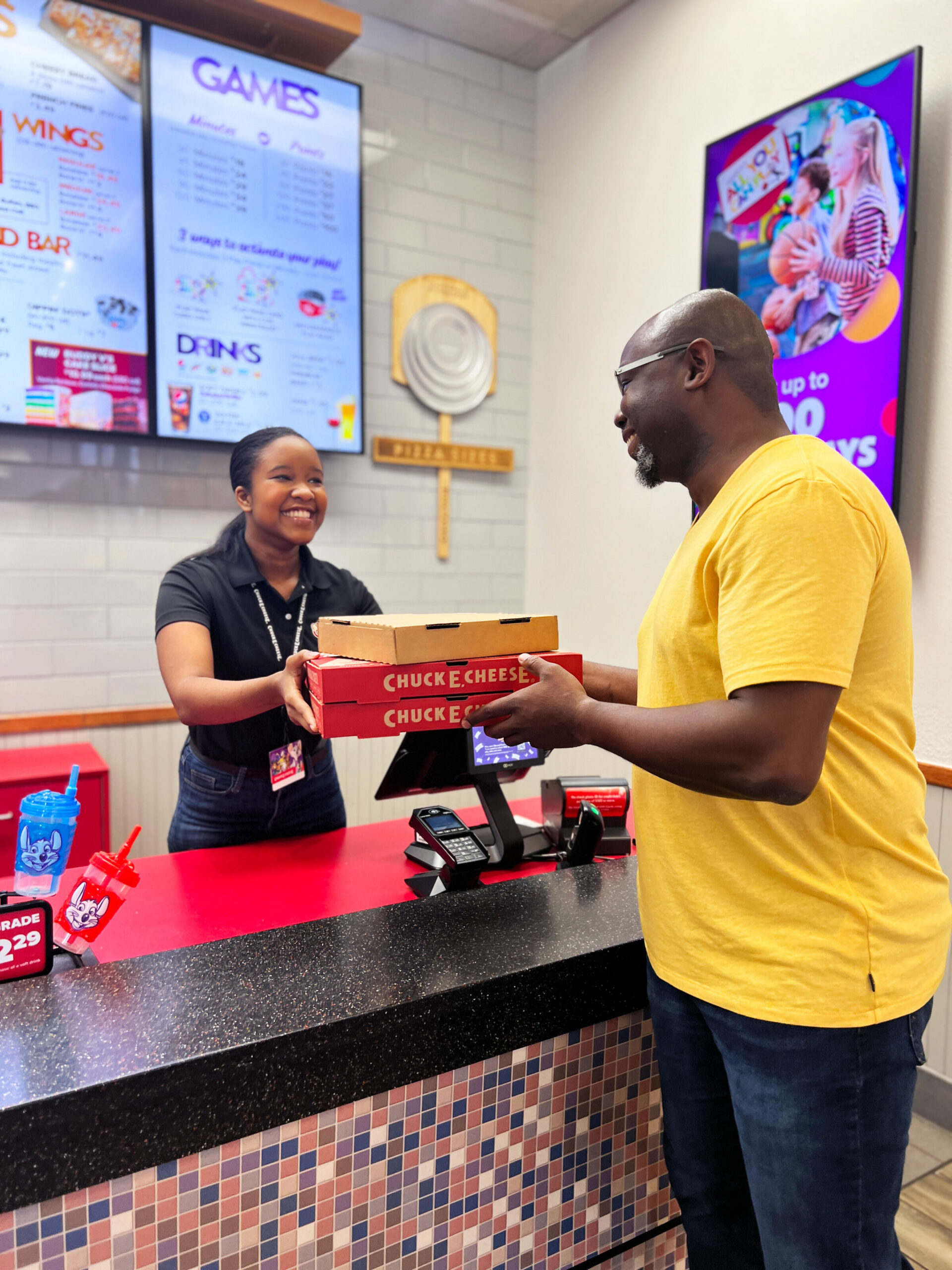 Chuck E. Cheese team member at the counter handing pizzas to a customer