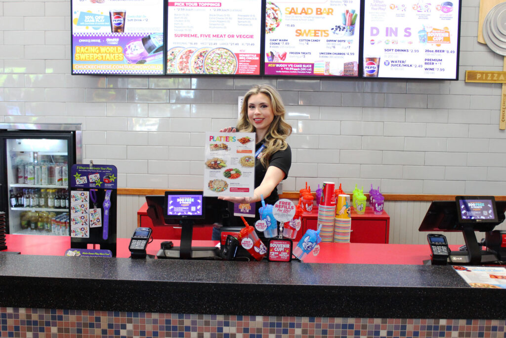 Chuck E. Cheese team member holding up a menu for platters at the counter.