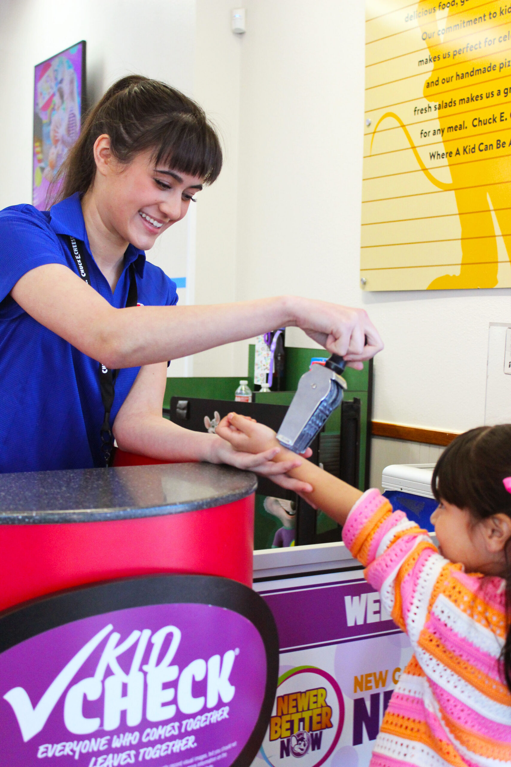 Chuck E. Cheese team member applying a Kid Check stamp to a child's hand at the entrance.