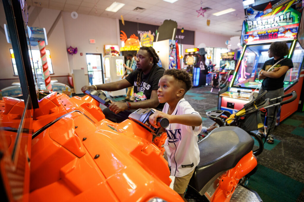 Father and son playing a racing arcade game together at Chuck E. Cheese.