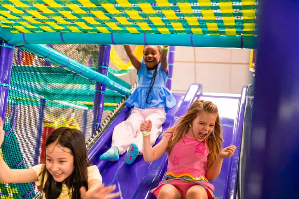 Three girls laughing as they slide down a purple slide