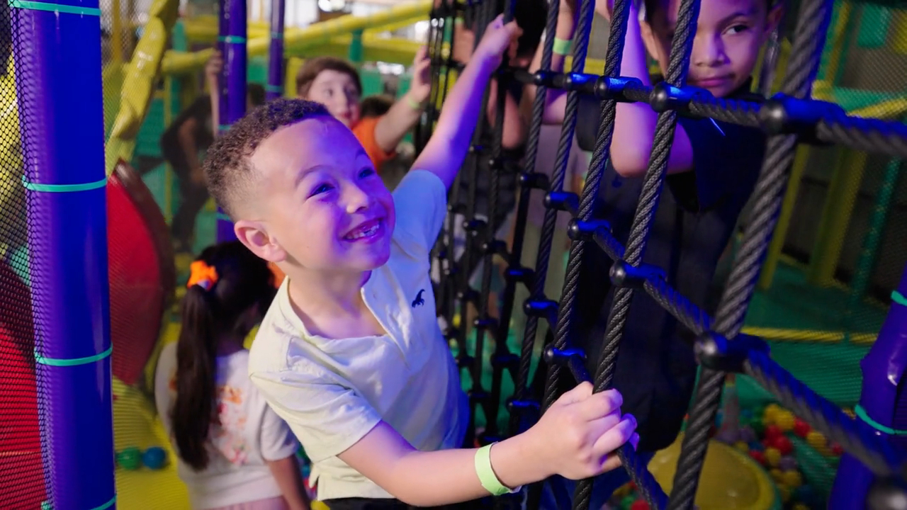 Kids playing with colorful climbing nets at Chuck E. Cheese, a multi-story Superhero Playground structure.