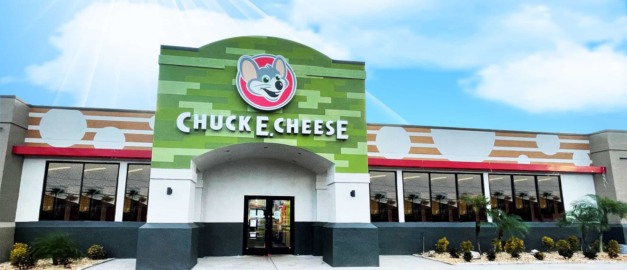 Exterior view of a modern Chuck E. Cheese building with a green facade and prominent logo, blue sky in the background.