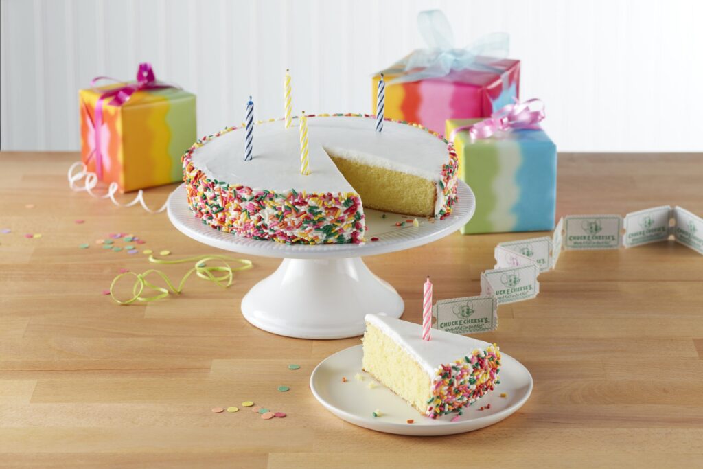 Birthday cake with candles in a Chuck E. Cheese party room, warm lighting and party decorations