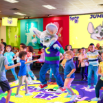 Chuck E. Cheese dancing with a group of kids on an interactive floor game at a Chuck E. Cheese location.