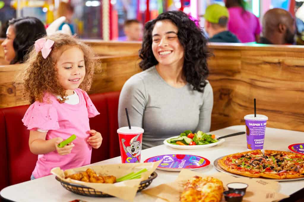 Mother and daughter enjoying pizza, wings and salad at a Chuck E. Cheese dining table