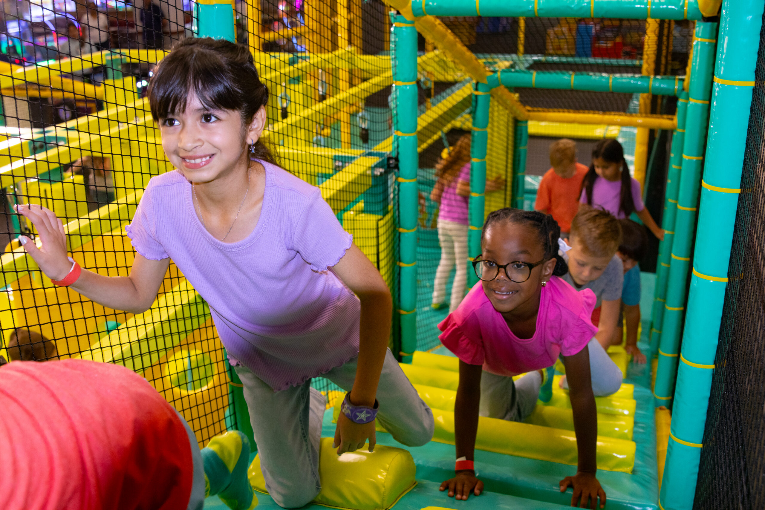 Kids smiling and crawling through a colorful play structure at Chuck E. Cheese Adventure World.
