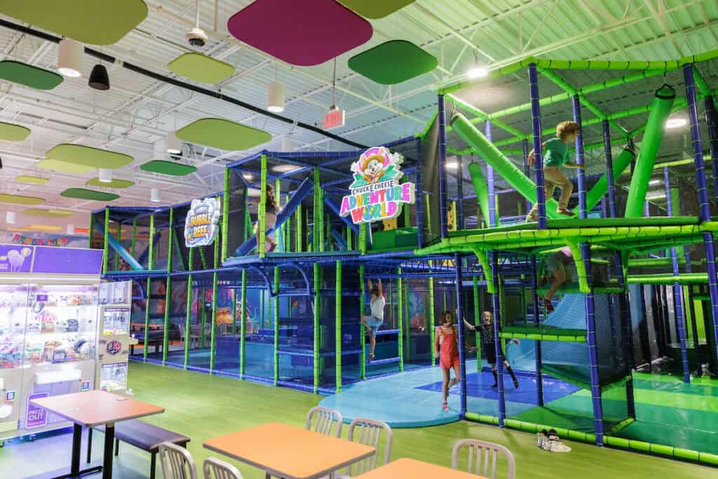 Kids playing and climbing in the multi-level Chuck E. Cheese Adventure World play structure.